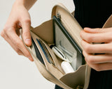 Close-up of a Metro Belt Bag in ivory (vegan leather) being opened, showing the organized interior with items like a tablet, cards, and other essentials neatly stored inside.